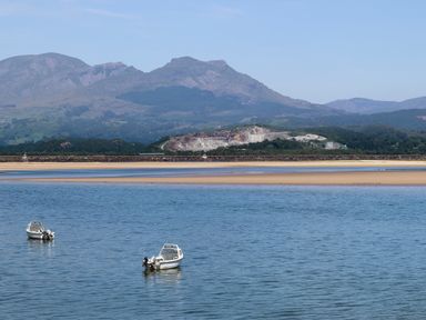 Two small boats on blue water with sandbars and mountains in the background at Bwthyn in Borth-y-Gest near Porthmadog