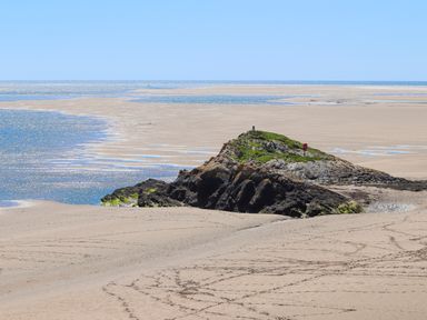 A sandy beach with a rocky outcrop covered in grass near the ocean at Bwthyn in Borth-y-Gest near Porthmadog