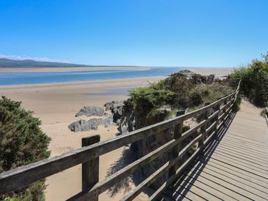 A wooden boardwalk next to sand dunes and water at Bwthyn in Borth-y-Gest near Porthmadog