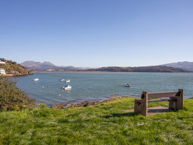 A bench on grass facing water with boats and hills in the distance at Bwthyn in Borth-y-Gest near Porthmadog