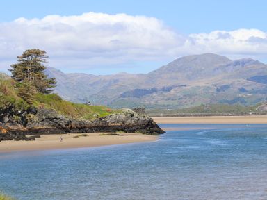 A coastal scene with sandy shore rocky cliffs trees and mountains in the background at Bwthyn in Borth-y-Gest near Porthmadog