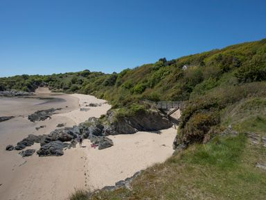 A sandy beach with rocks and a wooden bridge near green shrubs and hills at Bwthyn in Borth-y-Gest near Porthmadog