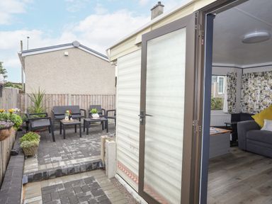 An outdoor patio area with chairs and tables and an open door leading to a living room at Rhiwlas Bach in Benllech