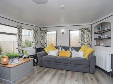 A living room with a gray sofa with yellow and white pillows and floral curtains at Rhiwlas Bach in Benllech