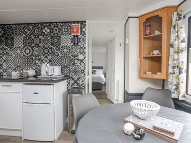 A kitchen area with a small fridge kettle toaster dining table and chairs with a view into a bedroom at Rhiwlas Bach in Benllech