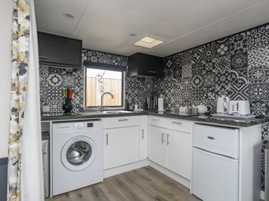 A kitchen with a washing machine a fridge a kettle toaster and patterned wall tiles at Rhiwlas Bach in Benllech