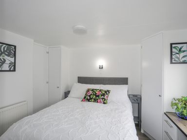 A bedroom with a bed white bedding and a floral pillow two nightstands two framed plant prints and a dresser with a plant at Rhiwlas Bach in Benllech