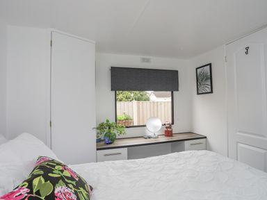 A bedroom with a bed a floral pillow a window with a gray blind a dresser with a mirror and decorations at Rhiwlas Bach in Benllech