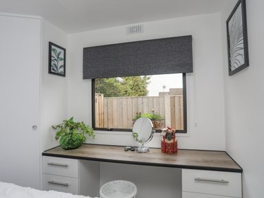 A desk with a round mirror, a green vase with plants, and gift boxes under a window with a grey blind at Rhiwlas Bach in Benllech