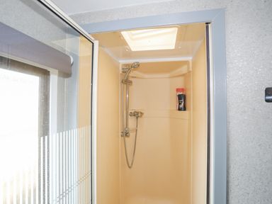 A shower area with a sliding glass door two bottles on a shelf a showerhead and controls at Rhiwlas Bach in Benllech