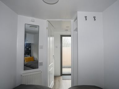A narrow bedroom with a mirror reflecting a bed with a yellow pillow and a door leading to a room with a frosted glass door at Rhiwlas Bach in Benllech