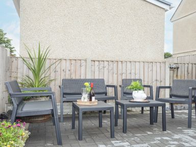 An outdoor patio with black chairs and tables two tables with plants and a bottle on one at Rhiwlas Bach in Benllech