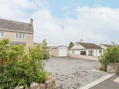 A paved driveway with green bushes and two houses in the background at Rhiwlas Bach in Benllech