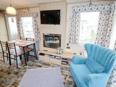 A living room with a blue armchair a wooden dining table with four chairs a wall-mounted tv and a fireplace at Beachcomber D35 in Towyn