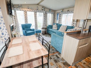 A living room with blue sofa armchair dining table and patterned curtains at Beachcomber D35 in Towyn