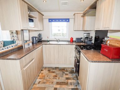 A kitchen with wooden cabinets a stove a sink and a window with a blue valance at Beachcomber D35 in Towyn