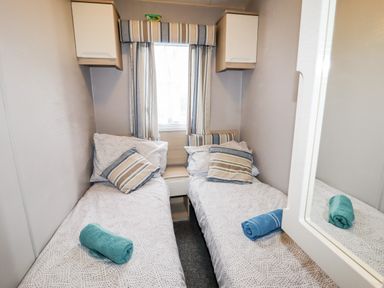 A bedroom with two single beds cushions and rolled towels next to a window at Beachcomber D35 in Towyn