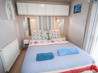 A bedroom with a double bed towels on the bed and storage cabinets above at Beachcomber D35 in Towyn