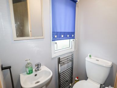 A small bathroom with a sink, mirror, toilet, window with blue blind, and a chrome towel radiator at Beachcomber D35 in Towyn