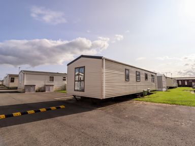 A row of mobile homes on paved and grassy lots under a partly cloudy sky at Beachcomber D35 in Towyn
