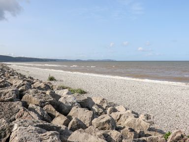 A rocky shoreline with a pebble beach and sea under a blue sky at Beachcomber D35 in Towyn