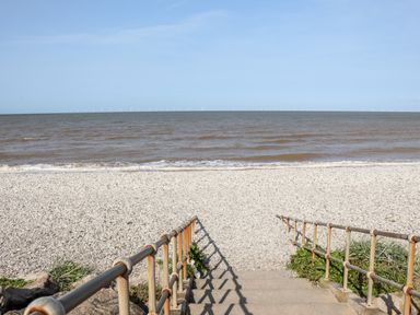 Concrete steps with metal railings leading down to a rocky beach with ocean and distant wind turbines on the horizon at Beachcomber D35 in Towyn
