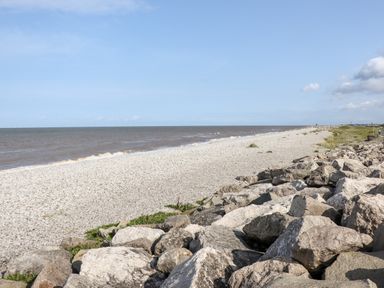A rocky shoreline with a pebble beach and sea under a clear sky at Beachcomber D35 in Towyn