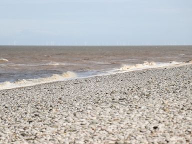 A pebble beach with waves crashing and wind turbines visible in the distance offshore at Beachcomber D35 in Towyn