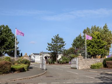 Entry gate to a holiday park with flags trees and paved road at Beachcomber D35 in Towyn