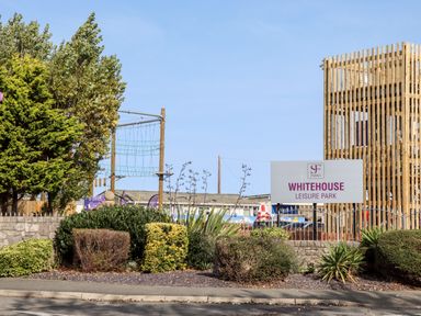An outdoor view of Whitehouse Leisure Park sign with bushes and wooden climbing structures in the background