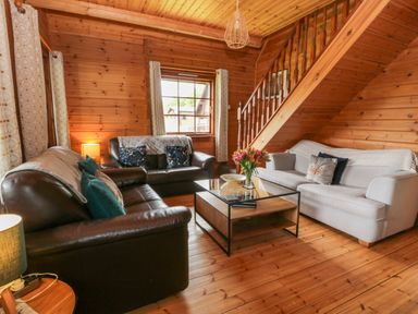A living room with two leather sofas one fabric sofa a wooden coffee table and a staircase at Glenisle in Dalbeattie
