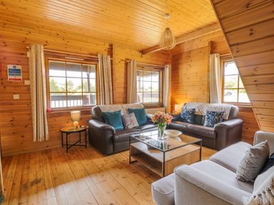A wooden living room with two leather sofas a fabric sofa a glass coffee table and a side table with a lamp at Glenisle in Dalbeattie