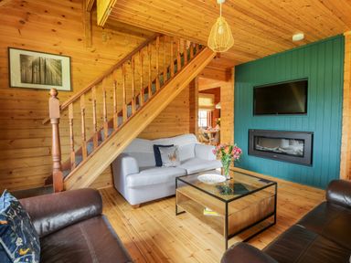 A living room with a wooden staircase a sofa a coffee table flowers and a fireplace at Glenisle in Dalbeattie