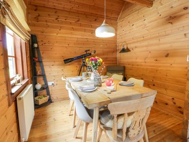 A dining area with a wooden table set with plates and a vase of flowers inside a wooden cabin at Glenisle Dalbeattie