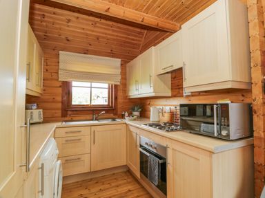 A kitchen with wooden cabinets and walls a window a microwave toaster and an oven at Glenisle in Dalbeattie