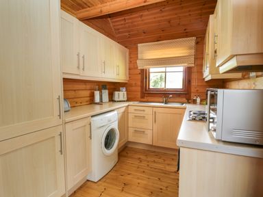A kitchen with wooden cabinets a washing machine a microwave and a window with a blind at Glenisle in Dalbeattie