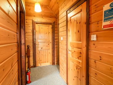 A hallway with wooden walls three wooden doors a hanging light and a fire extinguisher at Glenisle in Dalbeattie