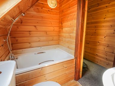 A wooden bathroom with a white bathtub toilet and handheld shower at Glenisle Dalbeattie