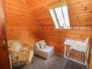 A wooden room with a wicker chair holding books and a pillow a gray star-patterned cushion with pillows a white high chair and a skylight window at Glenisle in Dalbeattie