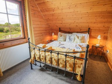 A bedroom with a black metal bed frame a window with yellow curtains and wooden walls at Glenisle Dalbeattie