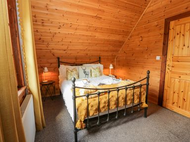 A bedroom with a metal bed frame wooden walls two bedside tables with lamps and yellow curtains at Glenisle in Dalbeattie