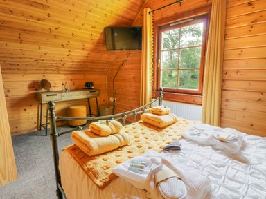 A bedroom with wooden walls and ceiling a bed with towels and bathrobes a desk with a stool and a mounted TV at Glenisle in Dalbeattie