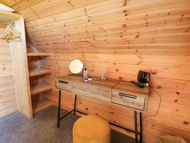 A wooden room with a desk holding a mirror and small items and an open shelving unit with hangers at Glenisle in Dalbeattie
