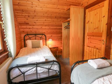A bedroom with two single beds wooden walls a small bedside table with a lamp and an open wardrobe at Glenisle in Dalbeattie