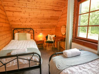 A bedroom with two single beds a bedside table with a lamp a chair with a cushion a dressing table and a window at Glenisle Dalbeattie
