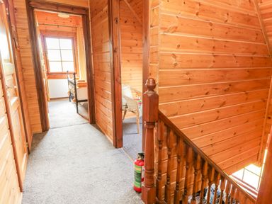 A wooden hallway with carpeted floor and stairs with a fire extinguisher near the railing at Glenisle in Dalbeattie