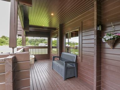 A covered wooden porch with a bench and hanging flowers at Glenisle in Dalbeattie