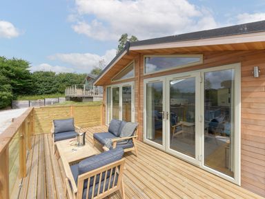 A wooden deck with outdoor furniture including chairs and a table outside a building with large windows and glass doors at 4 Valley View in Lanreath