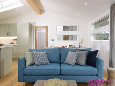 A living room with a blue sofa and cushions next to a kitchen and dining area at 4 Valley View in Lanreath