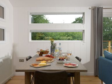 A dining table with food and drinks near windows and a blue sofa at 4 Valley View in Lanreath